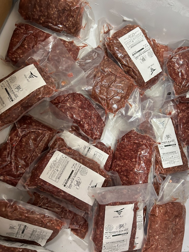 Vacuum-sealed packages of ground beef stacked in a cooler.